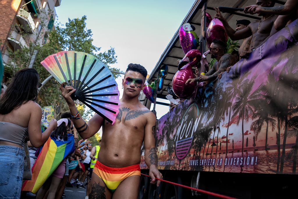 Un noi sense samarreta, un banyador amb els colors LGTBI i un ventall amb els colors de la bandera LGTBI, durant la manifestació del Pride! 2023.