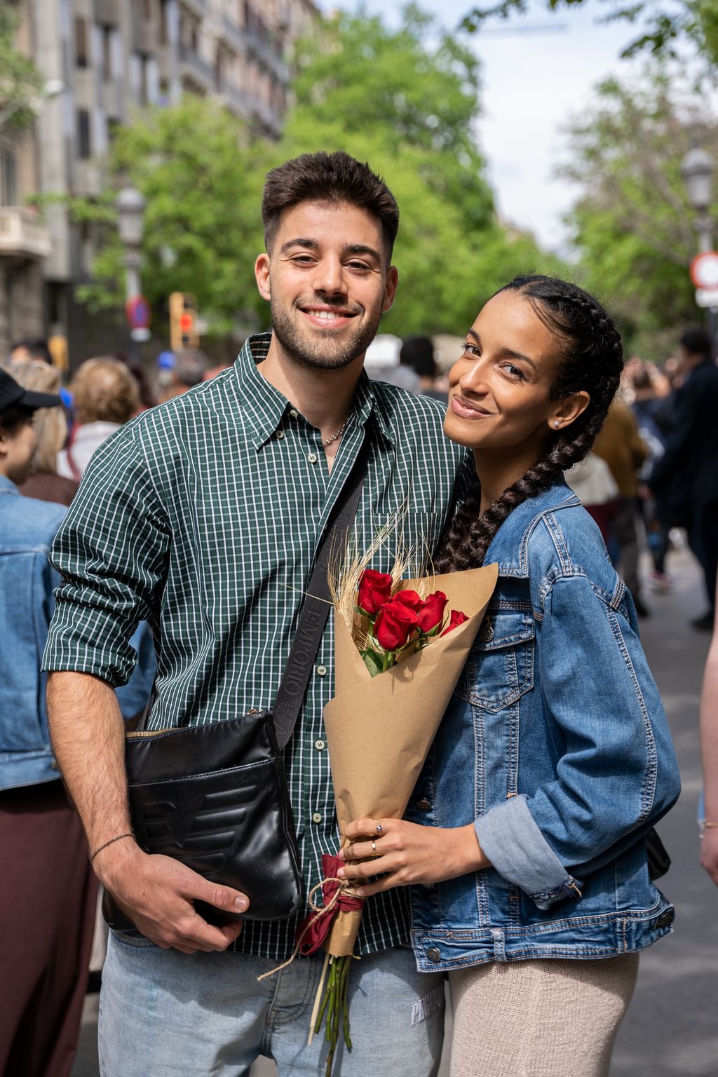 Retrat d'una parella jove a passeig de Gràcia el dia de Sant Jordi, amb la noia agafant un ram de roses vermelles.