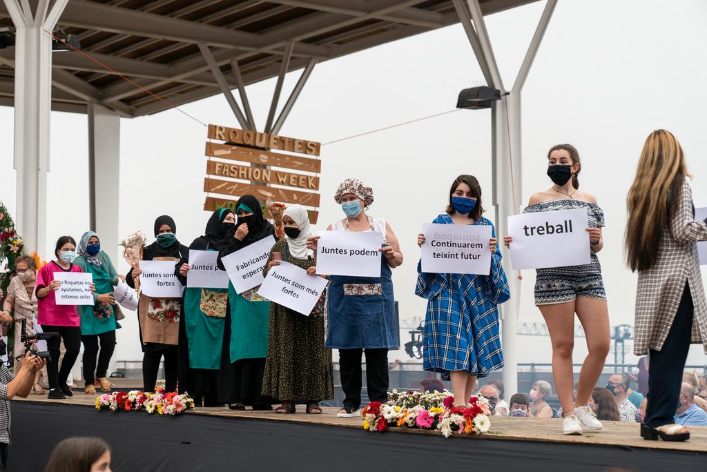 Final de la desfilada de la novena edició de la Roquetes Fashion Food & Wood Week amb unes dones mostrant cartells amb frases i paraules que tenen a veure amb el projecte de professionalització “Més amb menys”