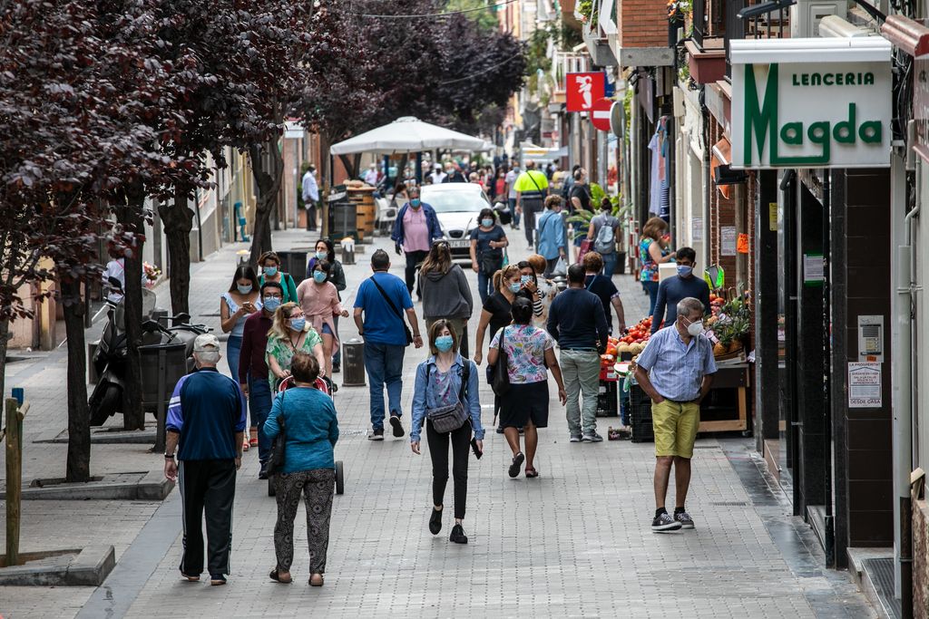 Vista general del carrer de Joaquim Valls amb gent de totes les edats anant i venint. Al voltant, els comerços estan oberts i hi ha veïns comprant