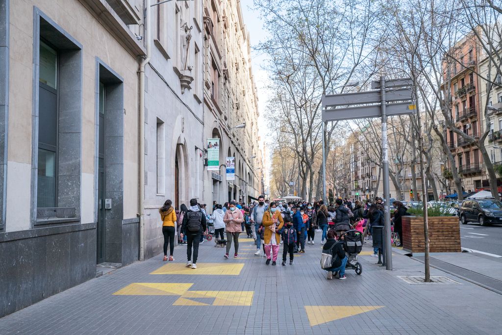 Les famílies passen a buscar els alumnes a la sortida de classe a l’Escola Pia Sant Antoni, a la ronda de Sant Pau. Davant de l’entrada s’ha ampliat la vorera ocupant un carril per construir-hi una plataforma de fusta que separa la zona del trànsit de vehicles, i a la vorera hi ha unes figures grogues