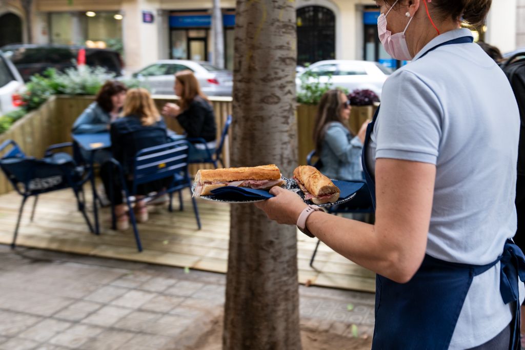 Una camarera llevando dos platos con bocadillos para unos clientes sentados en el exterior del restaurante, en uno de los nuevos prototipos de terraza