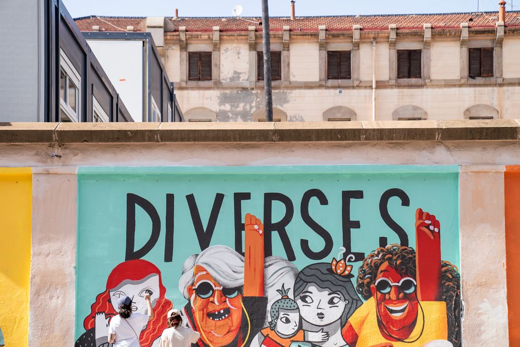 Cos central del mural reivindicatiu del mur exterior de la Model on es llegeix la paraula "Diverses" i que les il·lustradores estan acabant de pintar