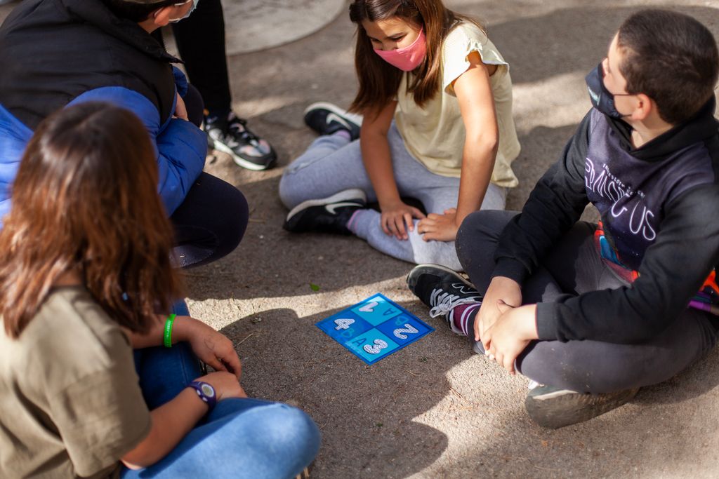 Grup de nens de l'Escola Mercè Rodoreda asseguts fent una rotllana durant una de les activitats d'una classe de matemàtiques en l'espai cedit a la plaça de Nou Barris
