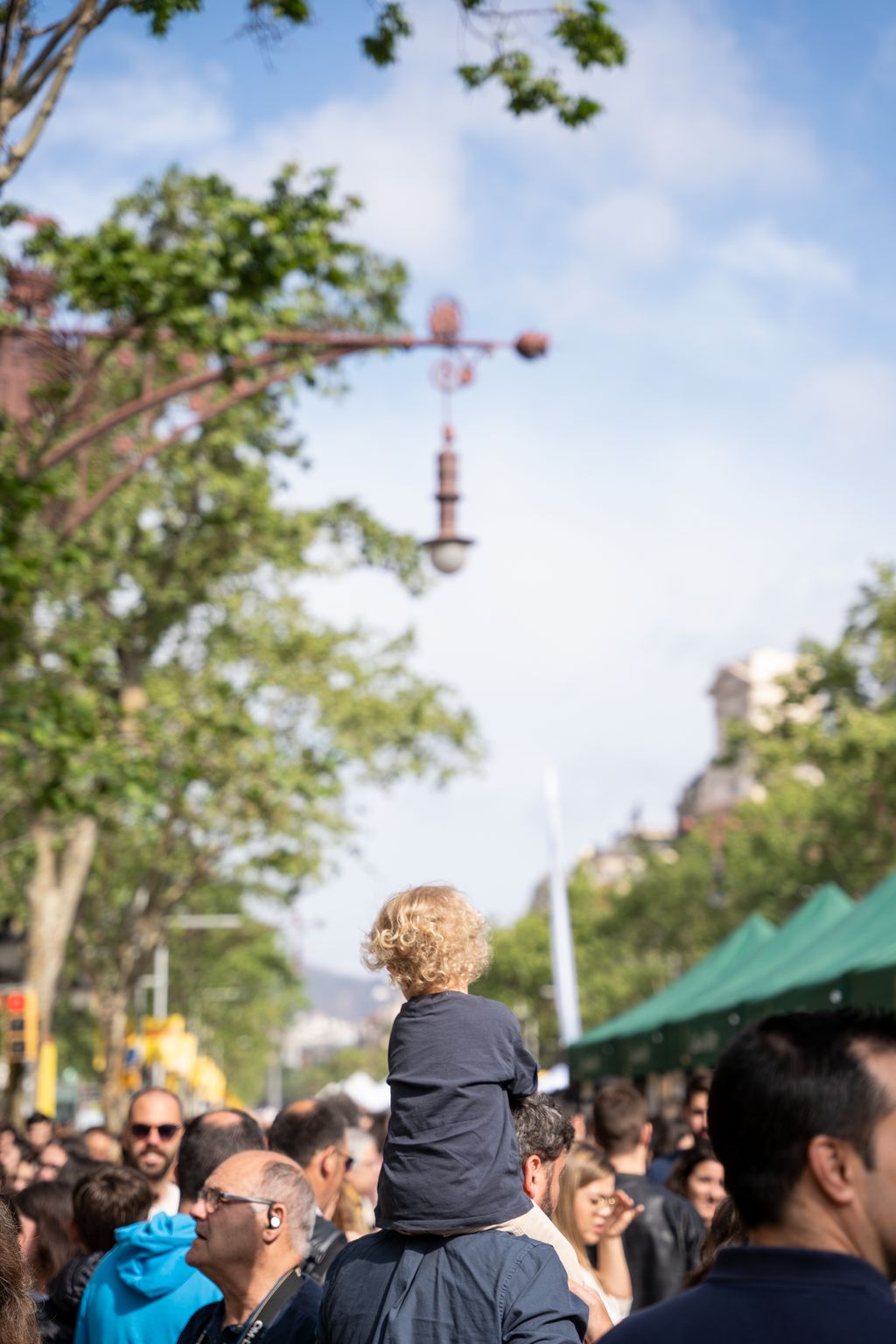 Una família amb un infant a coll passeja entre les parades de llibres i roses del passeig de Gràcia.