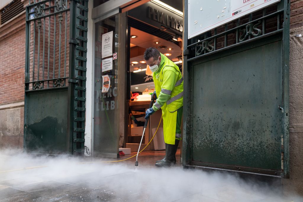 Un trabajador del Servicio de Limpieza limpia con vapor de agua el pavimento junto a uno de los accesos del Mercado de la Llibertat