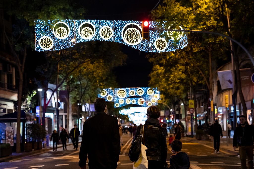 Una família passeja sota els llums de Nadal del carrer de la Creu Coberta aprofitant que està tancat al trànsit durant l’“Obrim carrers”