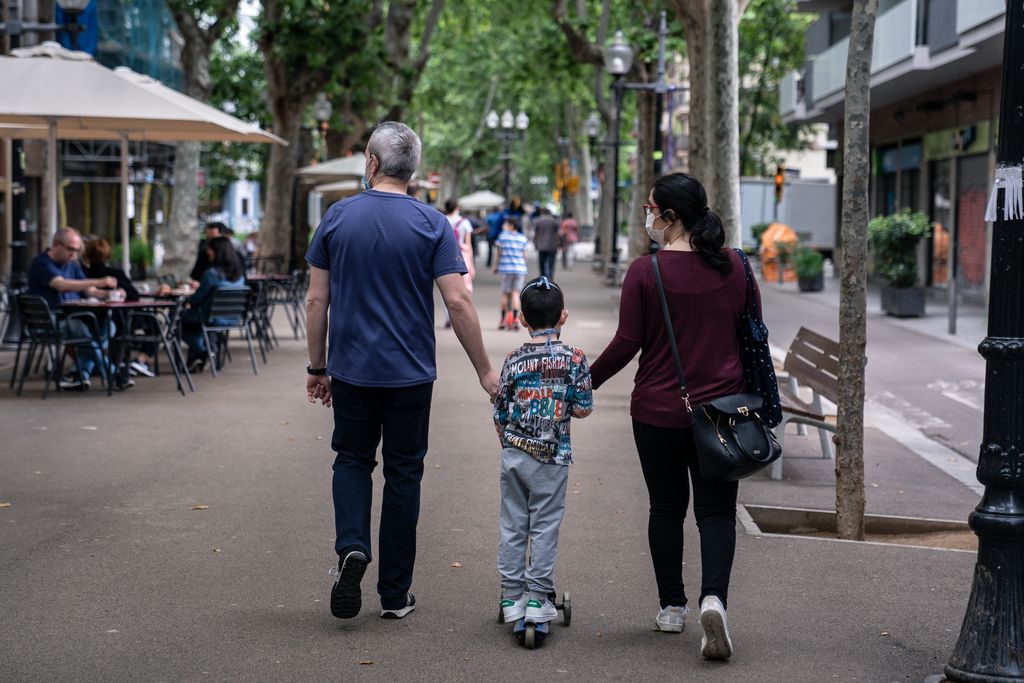Una família passejant amb el seu fill en patinet per la rambla del Poblenou. Hi ha gent asseguda a les terrasses