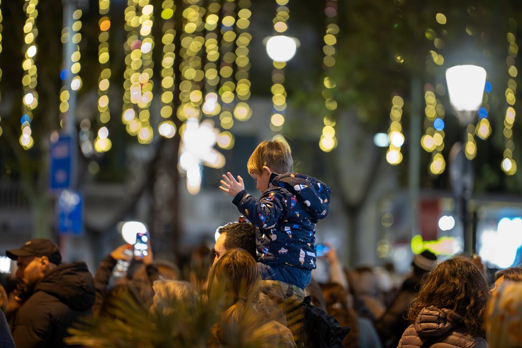Gent passejant i mirant els llums de Nadal i un nen a collibè el dia de la prova de l'encesa de llums