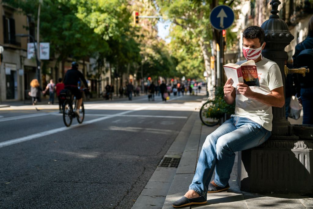 Un jove aprofita una font per seure a llegir al sol al carrer de Sants, tallat al trànsit per l'Obrim Carrers