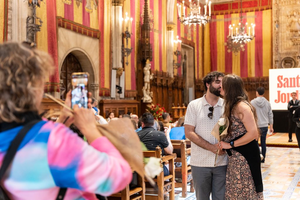Una parella es fa un petó al Saló de Cent mentre una dona els fotografia amb un telèfon mòbil
