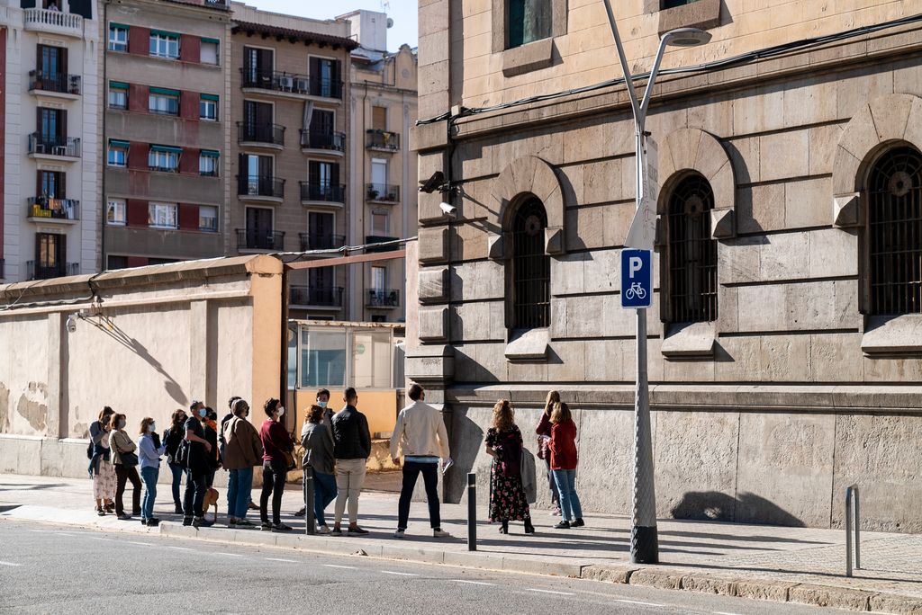 Grup de visitants aturats davant d'una porta d'entrada per a vehicles de l'antiga presó de la Model durant l'activitat "Passejos peripatètics: la por"