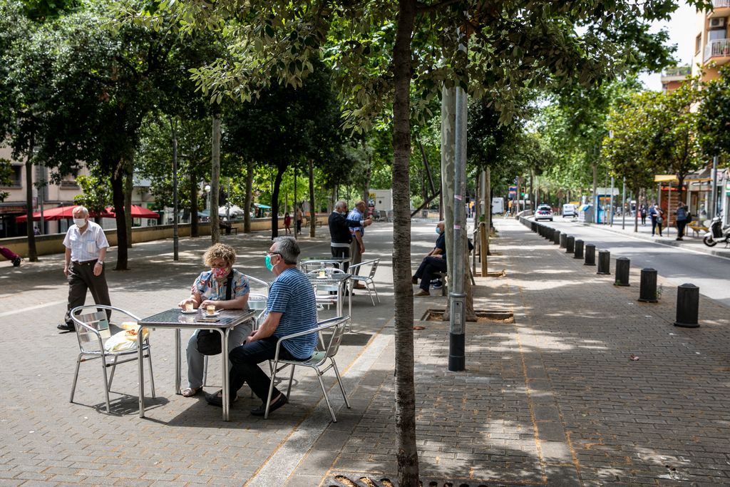 Una parella està asseguda en una terrassa de la via Júlia amb les mascaretes posades. Darrera, un grup d'homes grans conversa