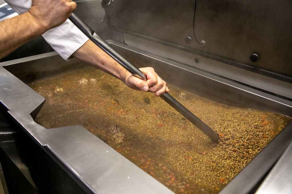 Un cuiner remena una gran olla industrial amb llenties