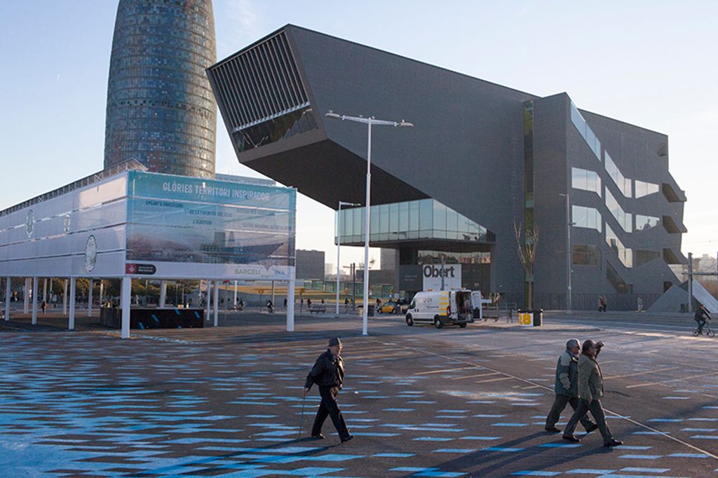 Persones creuant la Plaça de les Glòries Catalanes amb el Museu del Disseny i la Torre Glòries al fons