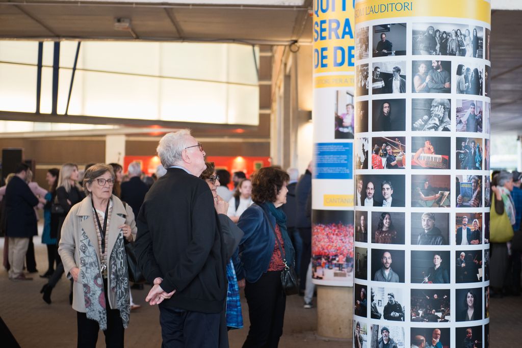 Gente mirando las imágenes de la exposición conmemorativa de los 25 años de L'Auditori.
