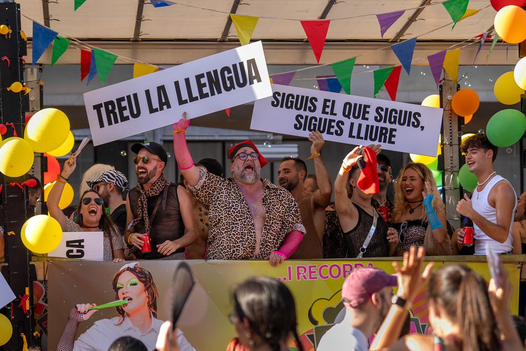 Ambient de la carrossa Allioli durant la manifestació del Pride! 2023. Dues persones alcen, cada una, un cartell amb els següents missatges:   La primera, “Treu la llengua”; la segona, “Siguis el que siguis, siguis lliure”.