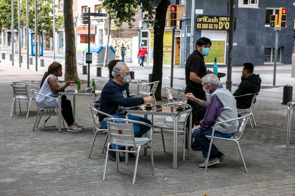 Unos hombres mayores con mascarillas sentados en una terraza a punto de tomarse el café que les acaba de traer el camarero