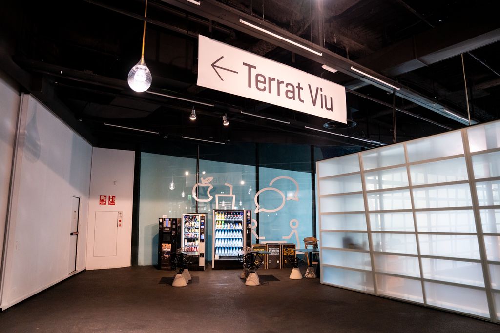 Zona de cafeteria del Museu de Ciències Naturals de Barcelona amb màquines distribuïdores automàtiques de begudes i menjar i taules amb cadires i un rètol indicador del “terrat viu”