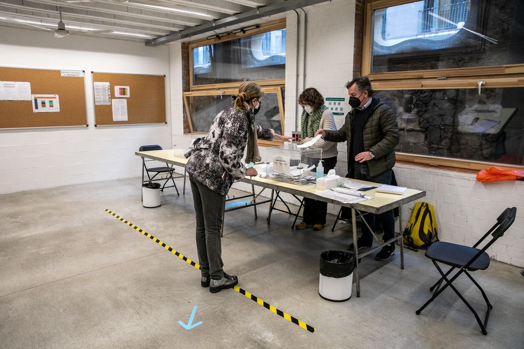 Una mujer vota en una de las mesas e intenta mantener la distancia de seguridad marcada frente a la mesa donde está situada la urna, en las Cristalerías Planell