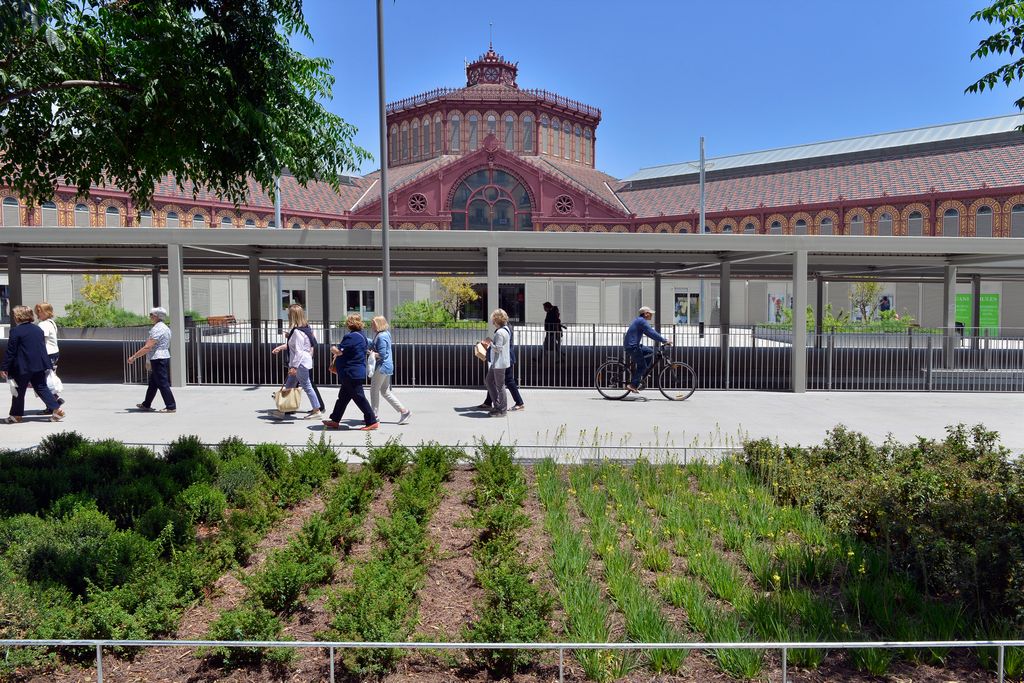 Veïns passejant per la zona pacificada de la superilla de Sant Antoni davant del mercat amb uns grans parterres amb plantes.