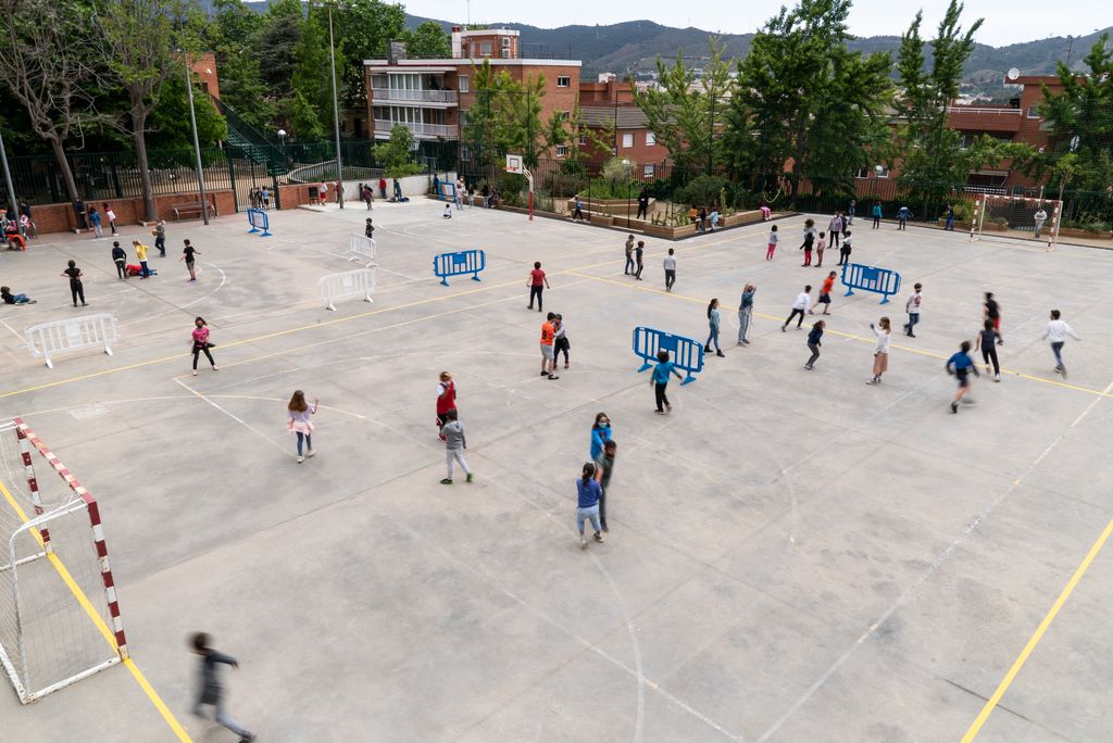Nens jugant a la pista de ciment del pati de l’escola amb tanques que diferencien diversos espais