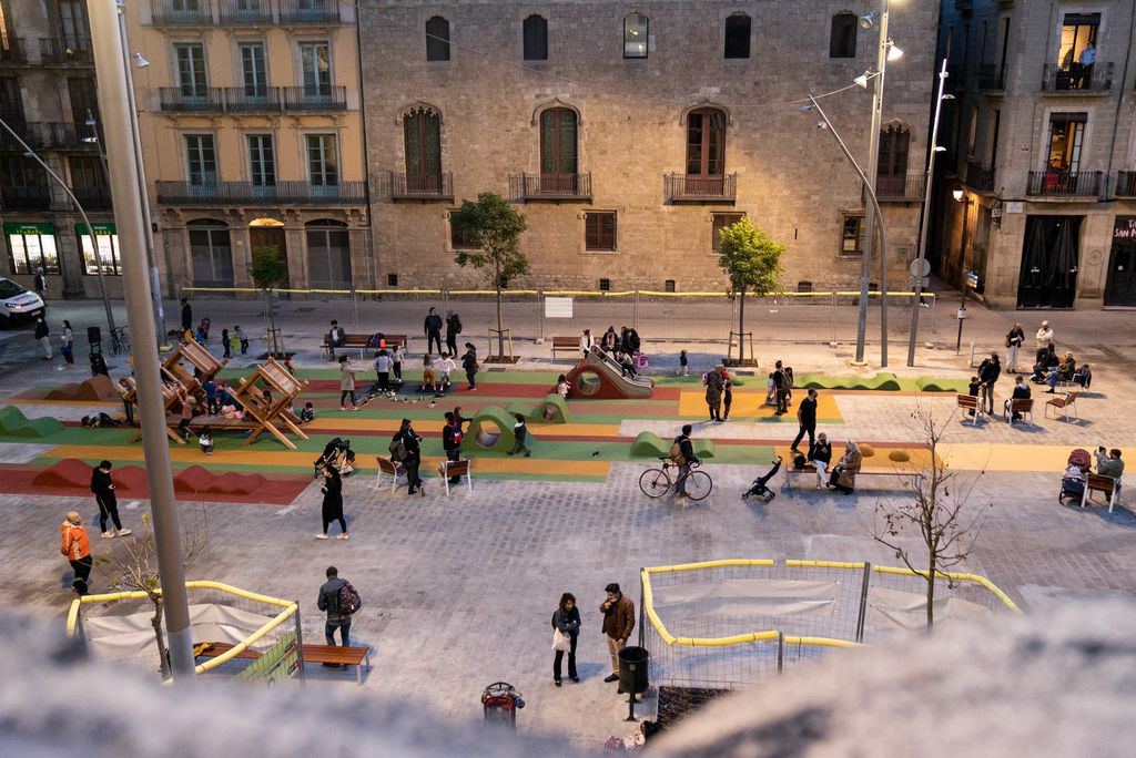 Vista de la plaça de Sant Miquel amb zones verdes i espai on es pot jugar. Hi ha moltes famílies jugant i veïns passejant