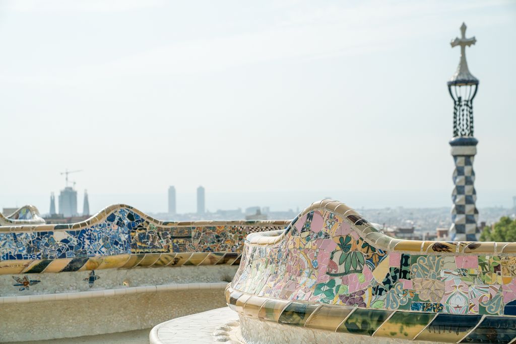 Plaça de la Natura amb el mirador sobre la ciutat delimitat pel banc ondulat de trencadís. Es veu la torre amb la creu gaudiniana del pavelló de la Porteria i al fons, alguns dels edificis emblemàtics del litoral