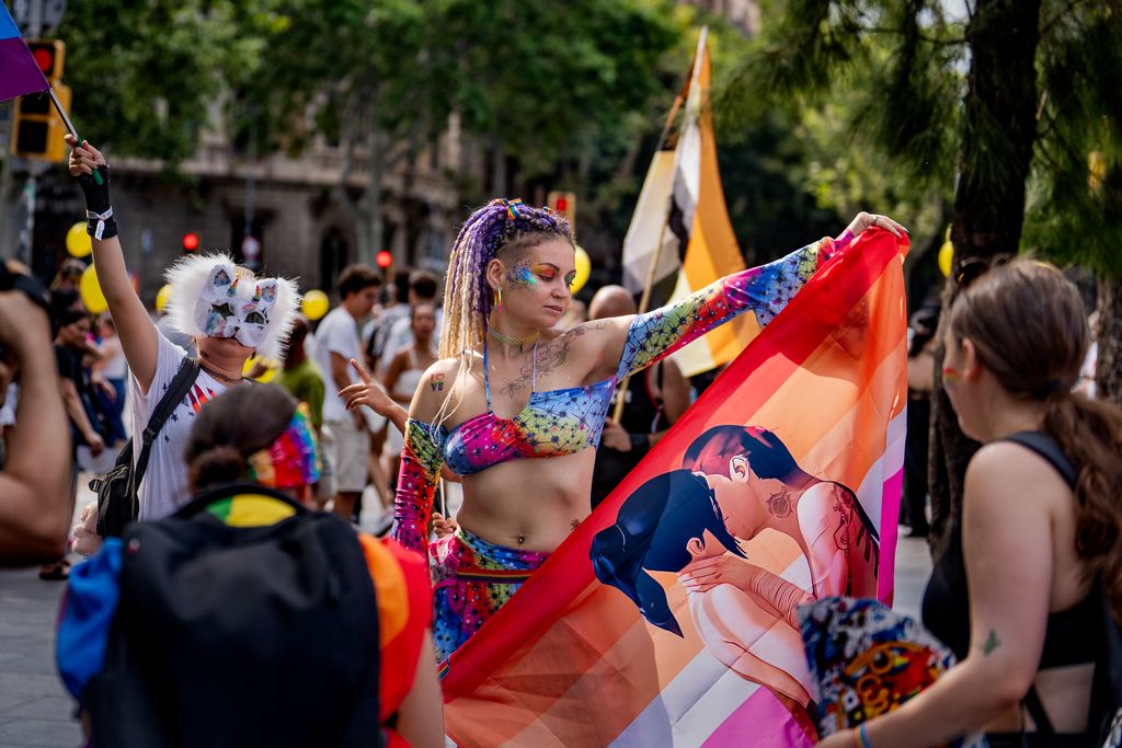 Dos personas, entre la multitud de gente en la manifestación del Pride 2025, posando para la foto, una enseñando la bandera lésbica y la otra con una máscara de gato con cuernos de unicornio