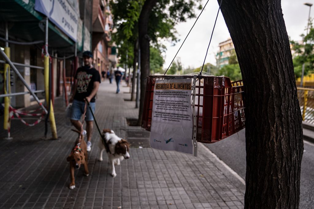 Caixa de recollida i donació d'aliments de l'Associació Luzazul a la rambla del Carmel. Al darrere, un home passeja els gossos