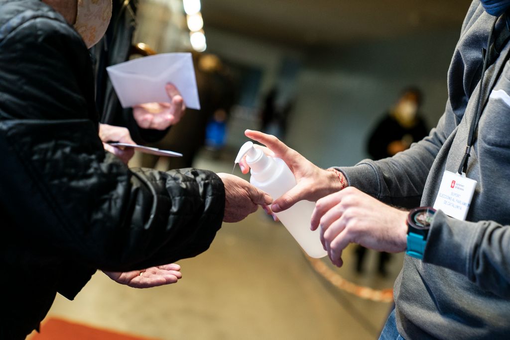Un treballador del dispositiu electoral posa gel hidroalcohòlic a les mans d'una votant que entra al col·legi electoral instal·lat al Poliesportiu Virrei Amat