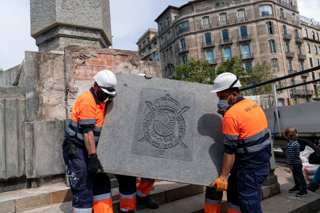 Els operaris retiren del monument de la plaça del Cinc d’Oros la placa amb l’escut dels Borbons per preparar-la per al transport