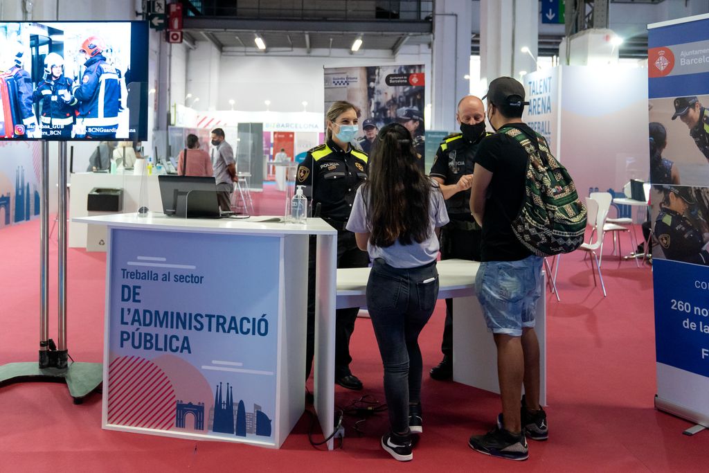 Dos joves demanen informació a l'estand de la Guàrdia Urbana durant la inauguració del BizBarcelona i el Saló de l'Ocupació
