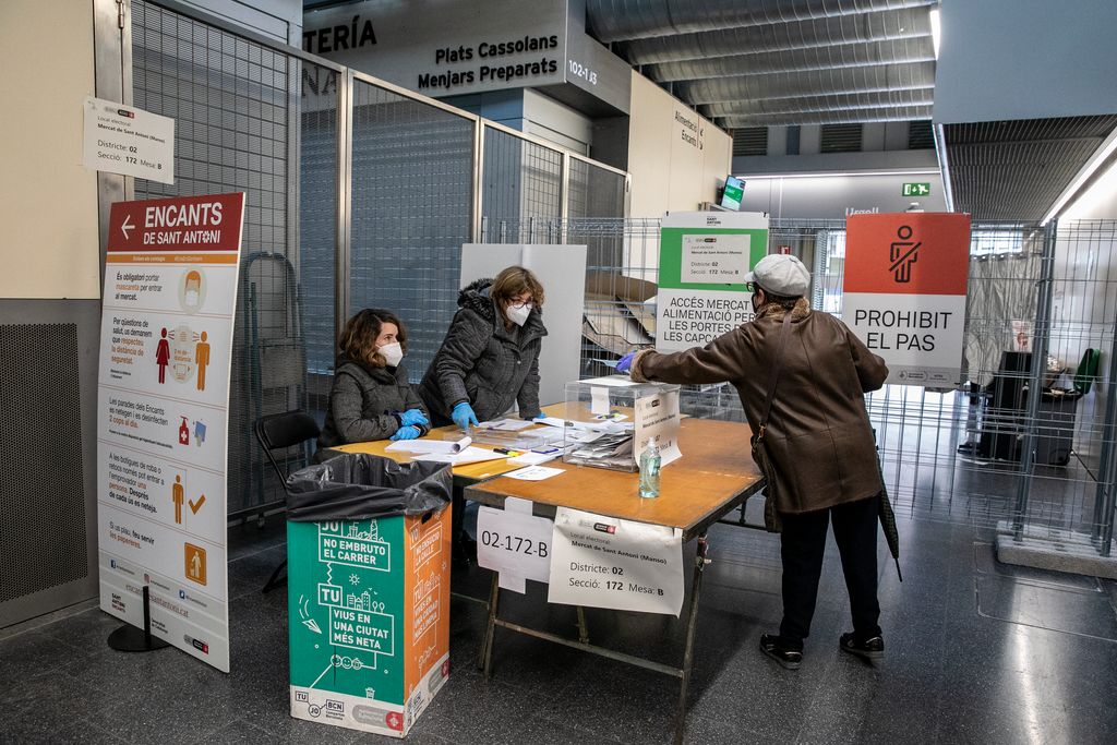 Una dona s'apropa a una mesa electoral instal·lada al Mercat de Sant Antoni i mostra la seva targeta censal