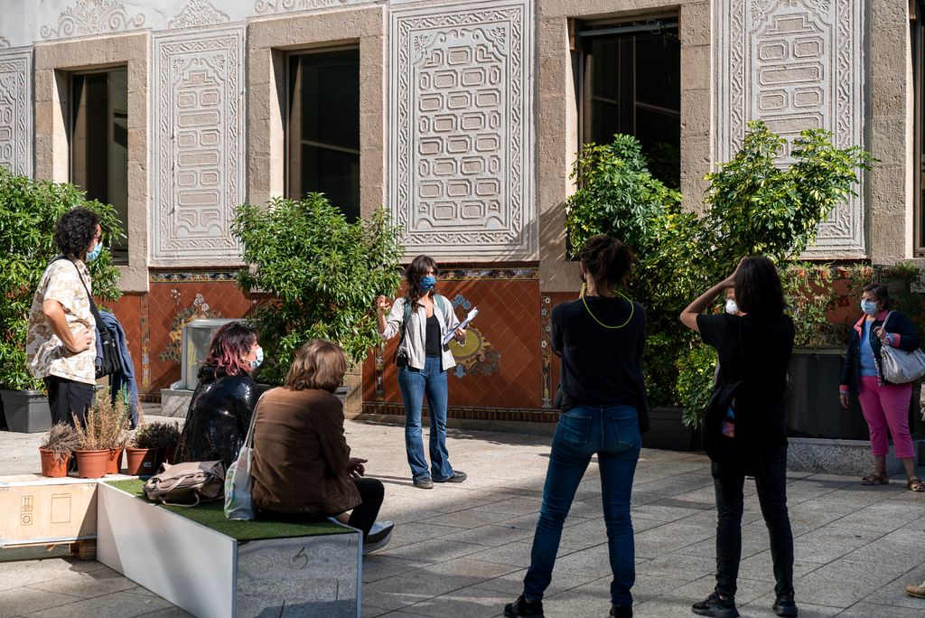 Els assistents a l'activitat de la Biennal de pensament "Passejos peripatètics: Reset", escolten les explicacions de la guia a la plaça de Joan Coromines