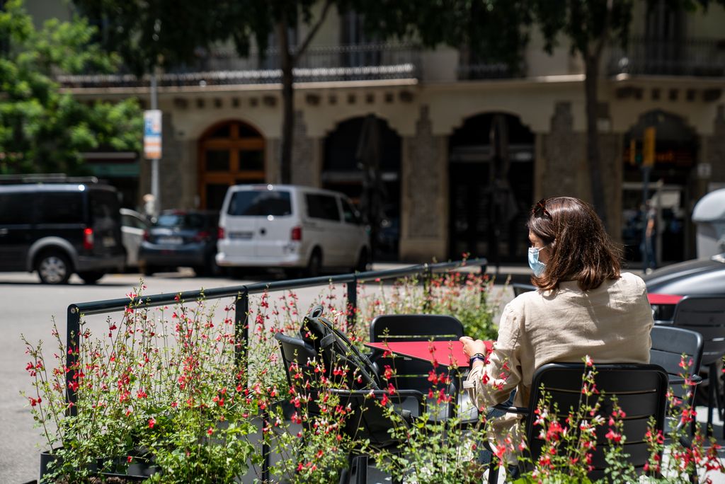Una dona seu davant una taula instal·lada sobre un nou prototip de terrassa en xamfrà separada del trànsit per unes baranes i per jardineres