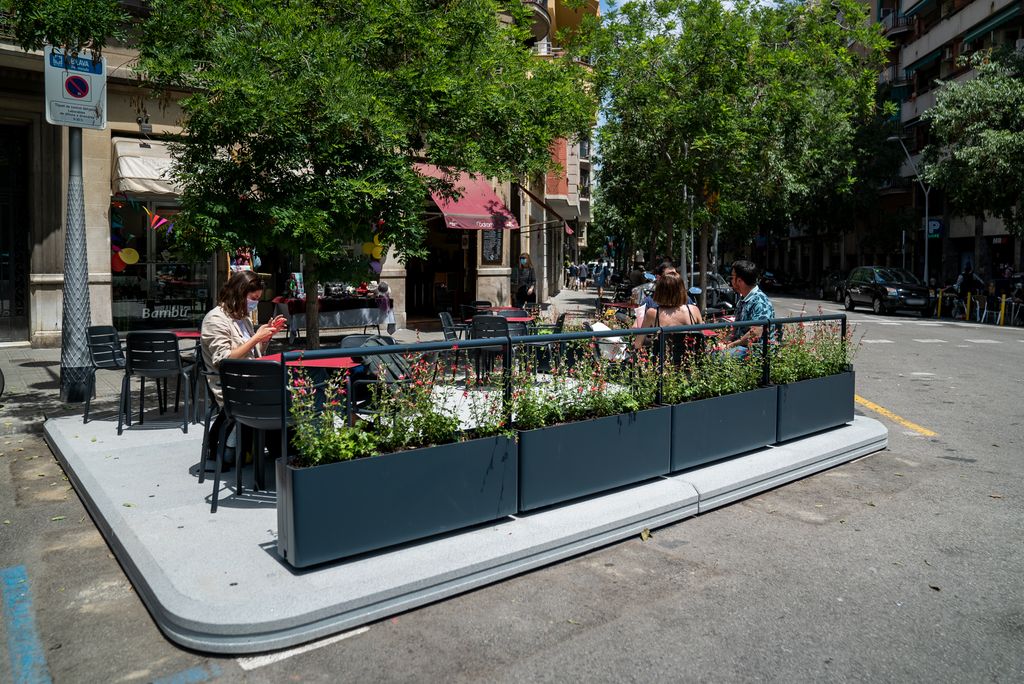 Clients asseguts a l’exterior d’un bar en un dels nous prototips de terrassa amb base de plaques de formigó i barreres laterals metàl·liques amb jardineres