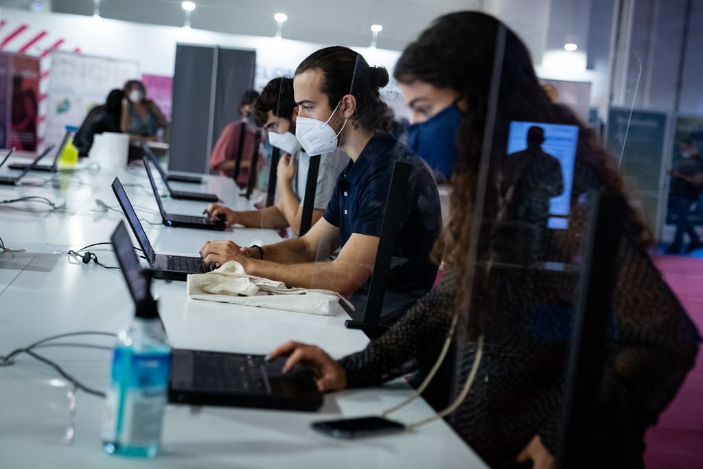 Assistents al Bizbarcelona i el Saló de l'Ocupació asseguts en una taula consultant els ordinadors portàtils; entre ells hi ha unes mampares i es veu gel hidroalcohòlic i altres materials per desinfectar