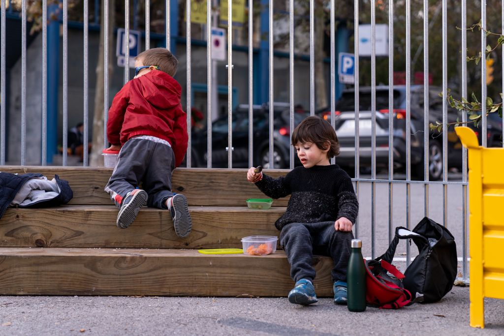 Uns nens aprofiten per berenar i jugar amb els seus ninos d’animals a la graderia de la zona pacificada a l’entorn de l’Escola Xirinacs