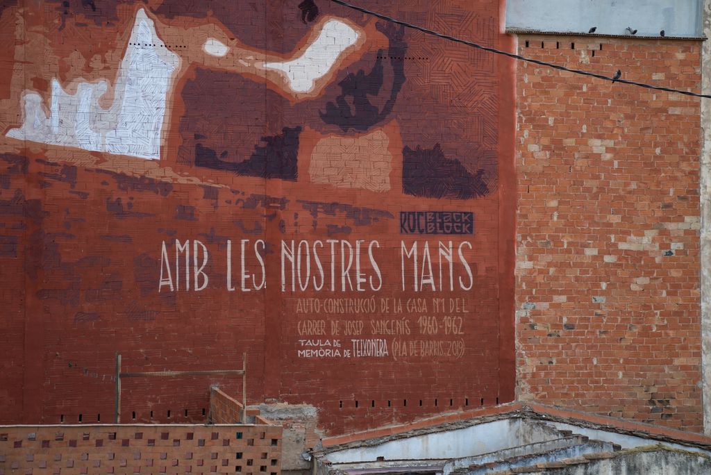 Part inferior del mural "Amb les nostres mans" en una mitgera del carrer de Sant Crispí, obra de Roc Blackblock, on s'hi pot veure el rètol commemoratiu i el nom de l'artista