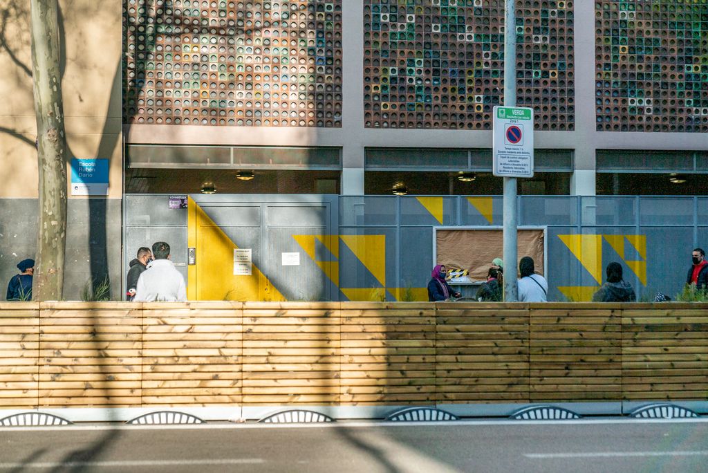 Famílies amb nens esperant a la zona pacificada de vorera ampliada davant de l’Escola Rubén Darío, on hi ha unes jardineres de fusta que separen la gent del trànsit