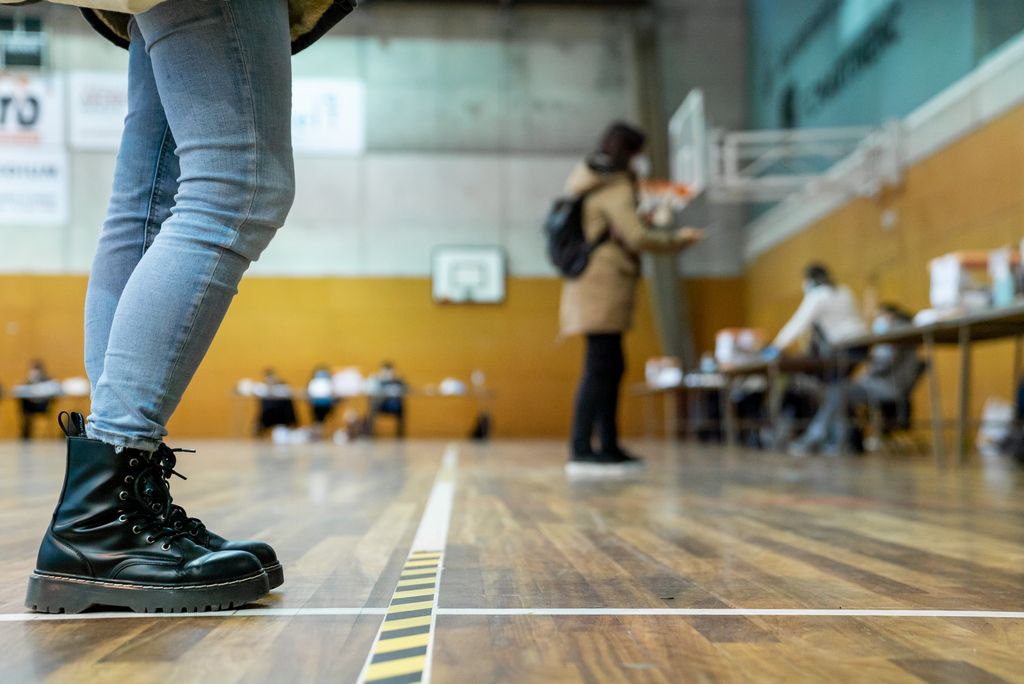 Una persona espera el seu torn dins del CEM Guinardó, per apropar-se a la mesa electoral on hi ha una altra persona que està votant