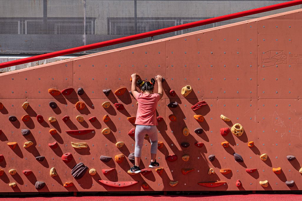 Una niña sube por un rocódromo de una plaza próxima a la Escuela La Pau