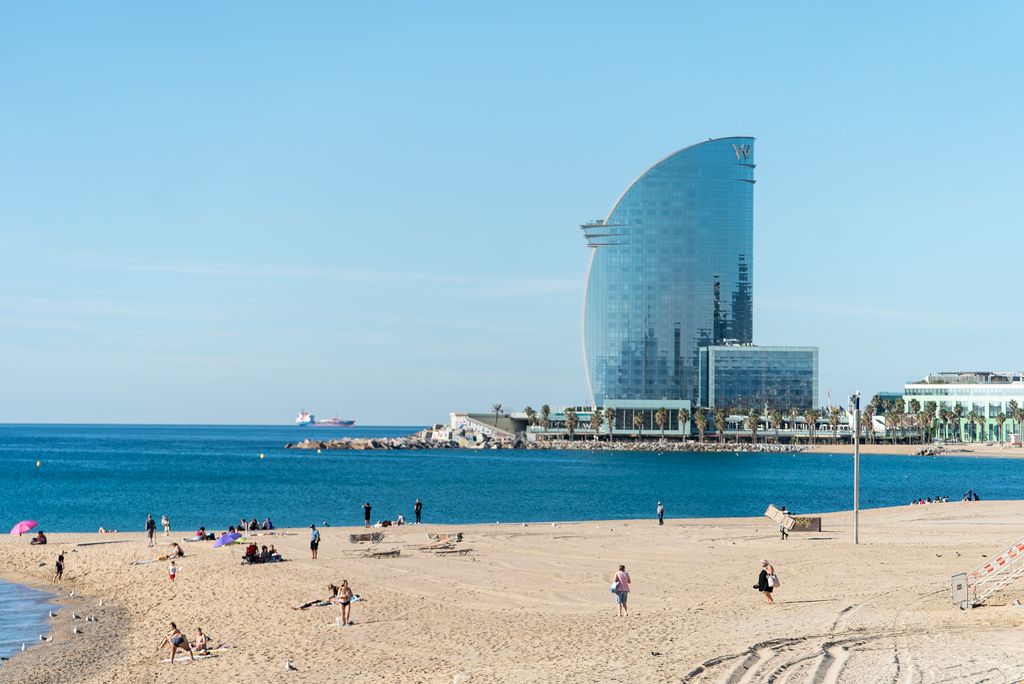 Banyistes arribant a la platja de la Barceloneta a primera hora del dia de Sant Joan un cop finalitzat l’operatiu especial de neteja Al fons, l’Hotel W