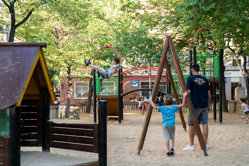 Nens acompanyats de les famílies jugant a l’àrea de joc infantil de la plaça de Comas