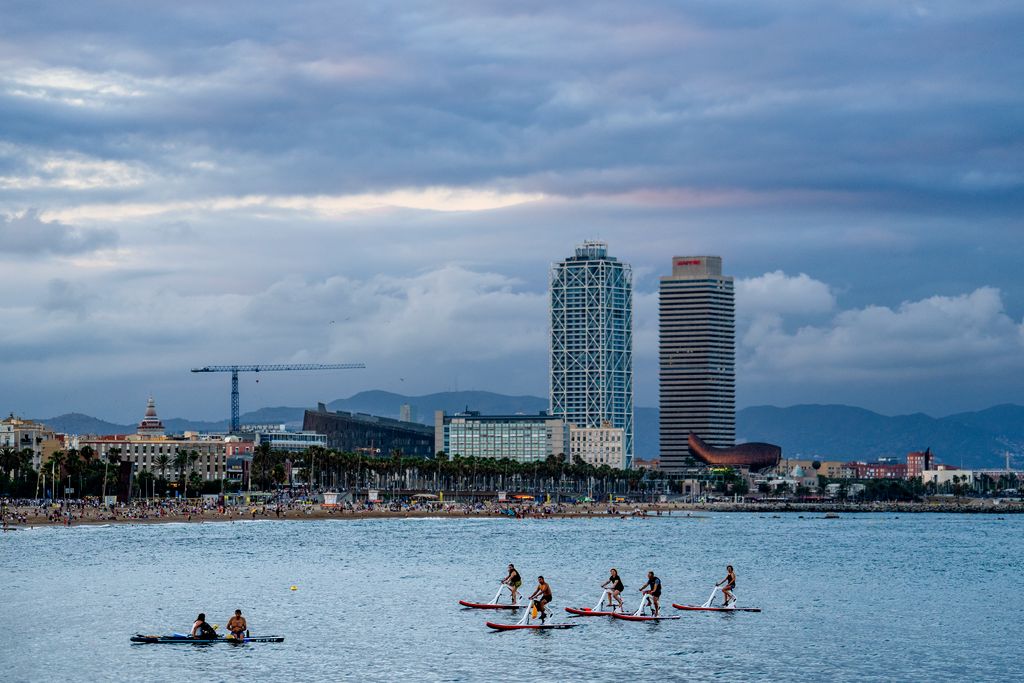 Grup de gent en 'bikesurf' a la platja de Sant Sebastià amb la Barceloneta i Nova Icària al fons