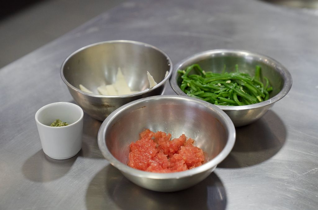 Conjunt d’ingredients preparats per a un plat: daus de tomàquet, verdura tallada a tires, formatge i salsa al pesto