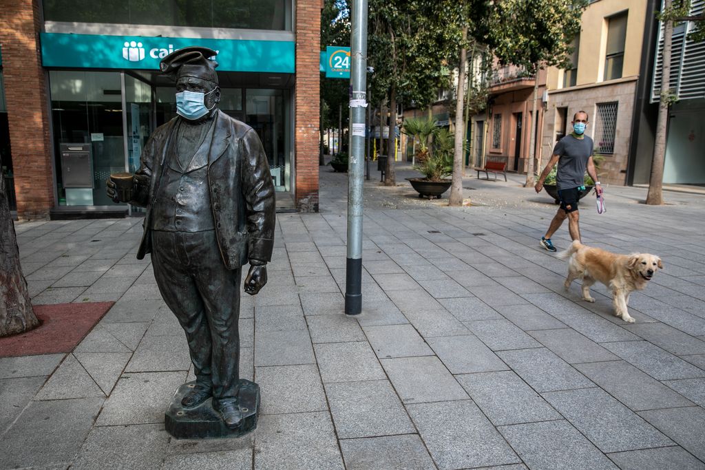 Escultura de "Pau Farinetes" amb una mascareta. Pel costat passa un home passejant el gos