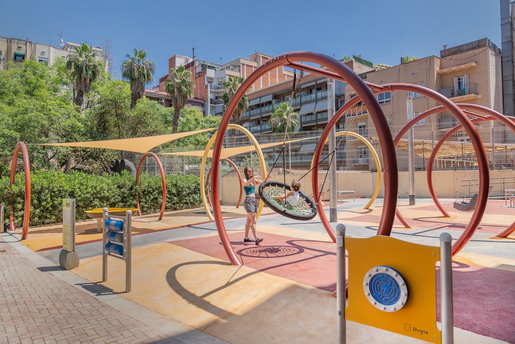Una mare juga amb el seu fill en un dels gronxadors de l'àrea de joc amb elements singulars accessibles i inclusius per a tots els infants dels jardins de Montserrat Roig