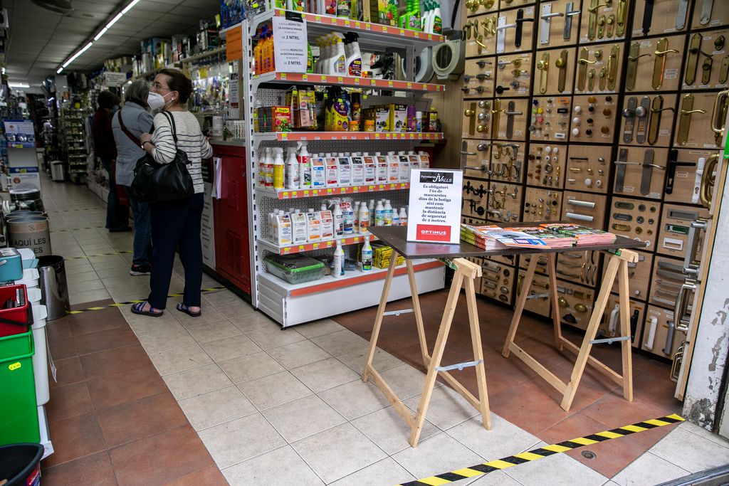 Gent comprant a una ferreteria del carrer Major de Sarrià esperant a la cua per ser atesos. A l'entrada hi ha un taulell que informa de les mesures de seguretat que cal seguir